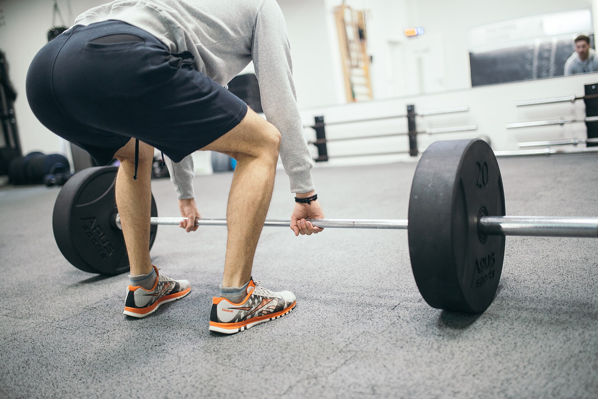 Eine Person richtet sich in einem Fitnessstudio für Kreuzheben mit der Langhantel ein.